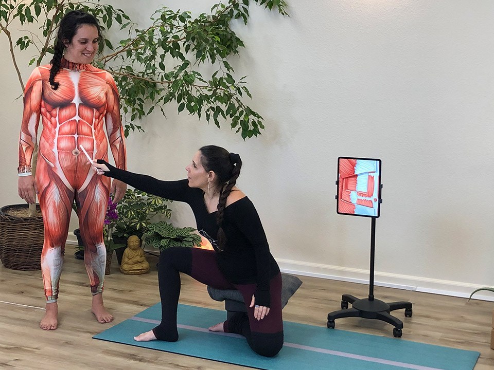 Jennifer More points to a group of muscles on her student, who is wearing an anatomical representation of the abdominal muscles. Jennifer is teaching how diastasis recti occurs and how to prevent the separation of the muscles.